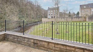 A courtyard with a stone wall, a metal fence, and a grassy area with trees. - Host & Stay | 57 Woodland View (Holmfirth)