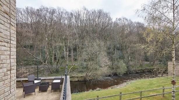 A patio area with outdoor furniture, a brick wall, and a view of a river and forest. - Host & Stay | 57 Woodland View (Holmfirth)