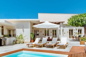 Un espace aménagé au bord de la piscine, avec des chaises longues, un barbecue et des plantes en pot.