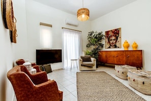 Sala de estar com televisão, sofá, poltrona e aparador com objetos decorativos.