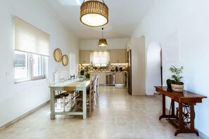 A modern kitchen with a central island, pendant lighting, and a dining area with a long table.