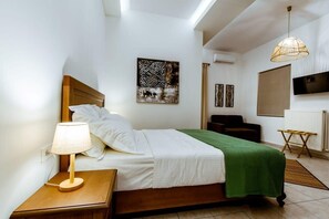 Ein ordentlich eingerichtetes Schlafzimmer mit Bett, Nachttischlampe, Kunstwerken und einem Fernseher an der Wand.