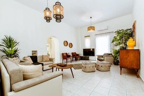 A spacious living room with a sofa set, a coffee table, and a TV. There are wicker baskets and a wooden cabinet.