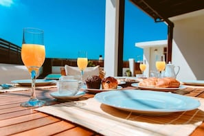 Ein Frühstückstisch mit Orangensaft, Muffins und Croissants, mit Blick auf ein Gebäude und einen klaren Himmel.