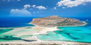 An aerial view of a coastal area with a prominent rocky island, clear turquoise waters, and a sandy beach.