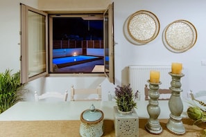 Une chambre avec vue sur une piscine illuminée la nuit, une table blanche agrémentée d’objets décoratifs et deux assiettes décoratives fixées au mur.