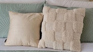 Un lit recouvert d’une couvre-lit à motifs verts, deux reproductions encadrées de plantes ornant le mur, et une variété d’oreillers.