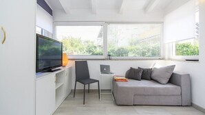 Un salon moderne avec un canapé gris, un fauteuil noir, un téléviseur et un ordinateur portable posé sur un meuble blanc.