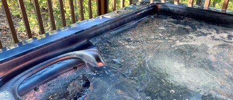 A hot tub with water, surrounded by wooden deck railings and greenery.