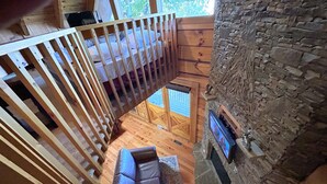 Interior de una cabaña de madera con un altillo, una chimenea de piedra y un sofá de cuero.
