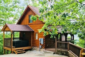 A wooden cabin with a porch and hot tub, surrounded by trees. - Love Shack honeymoon cabin that is stairway to the stars! (Sevierville)