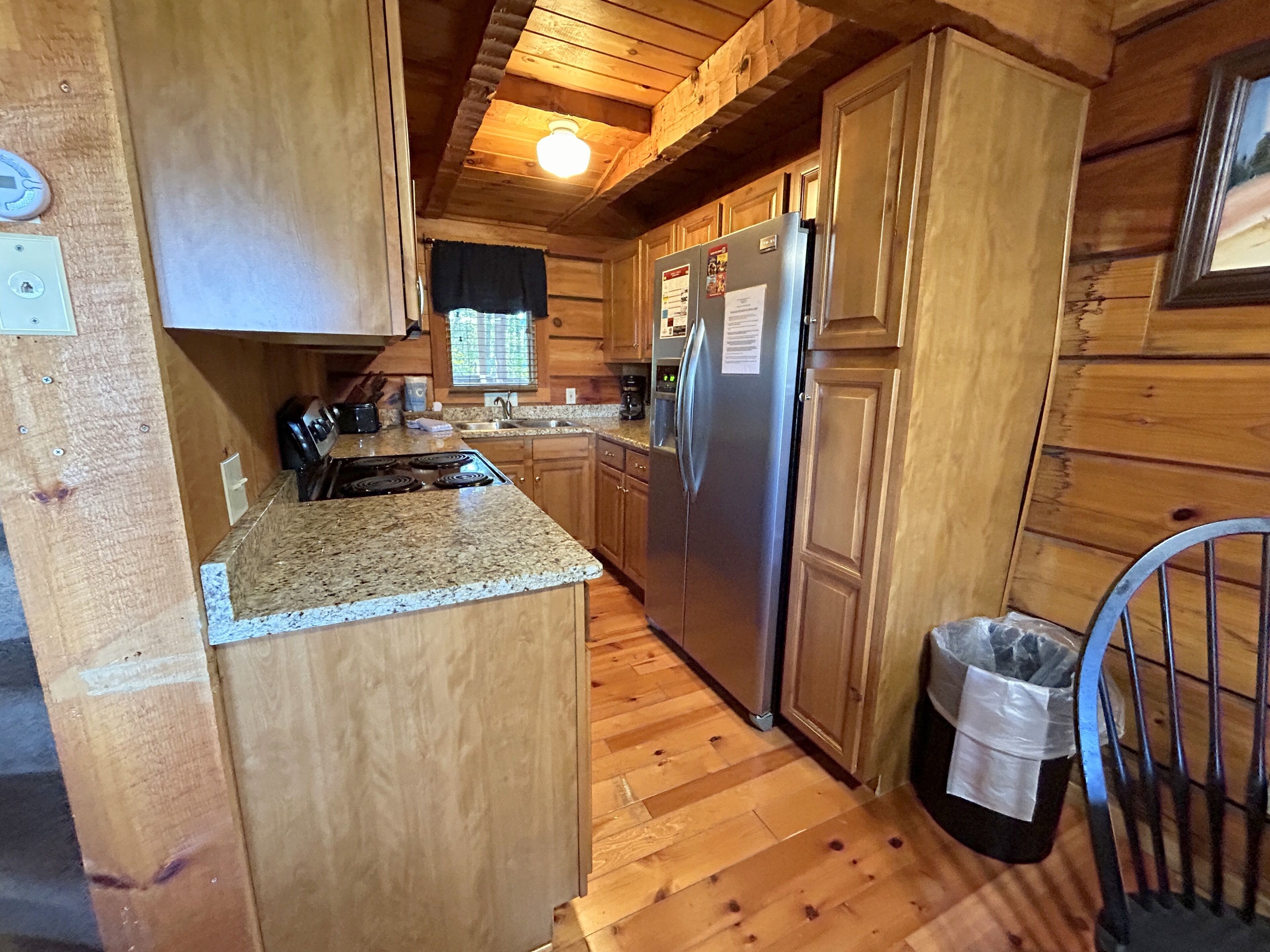 A wooden cabin kitchen with granite countertops, a stainless steel refrigerator, and a wooden floor.