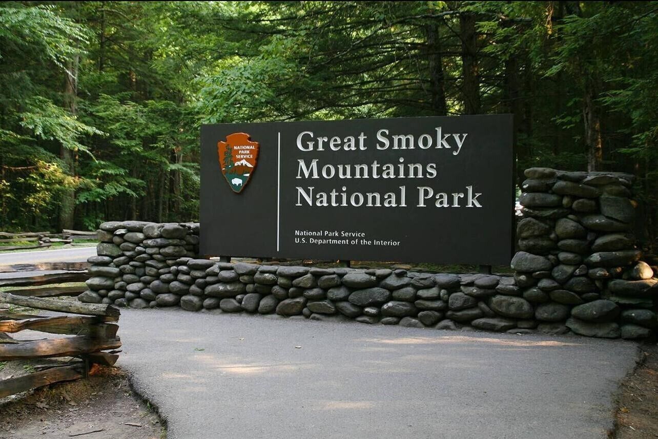 A sign for Great Smoky Mountains National Park with a stone wall and wooden fence in the background.