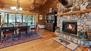L’intérieur chaleureux d’un chalet avec une cheminée en pierre, un plafond en bois et un coin repas comprenant des chaises et une table.