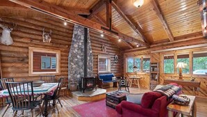 L’intérieur d’une cabane en rondins, avec une cheminée en pierre, des meubles en bois et un coin salon confortable.
