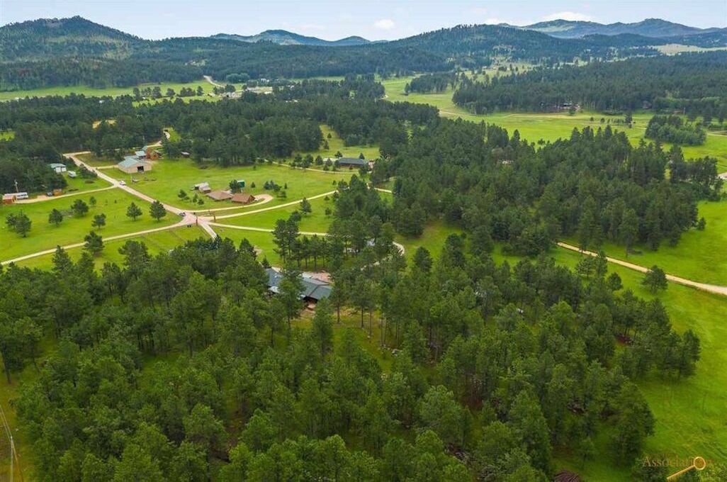 An aerial view of a rural area with scattered buildings, roads, and dense forests.