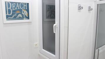 Un baño con cabina de ducha, un cuadro enmarco con una escena de playa y un perchero para toallas.