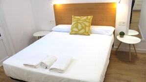 Ein ordentlich bezogenes Bett mit weißen Leinentüchern und zwei aufgerollten Handtüchern, ein Holz-Kopfteil und ein kleiner Nachttisch mit einer Pflanze.