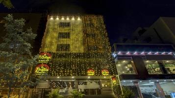 Fachada de hotel iluminada en la noche, con luces de adorno y un letrero llamativo que dice 'The Bistro', y una entrada visible.