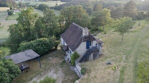 Een traditioneel stenen huis met rieten dak, omgeven door een grasveld en bomen.