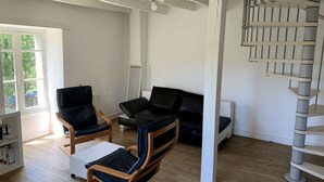 Ett modernt vardagsrum med en svart lädersoffa, en trästol, ett vitt soffbord och en spiraltrappa.