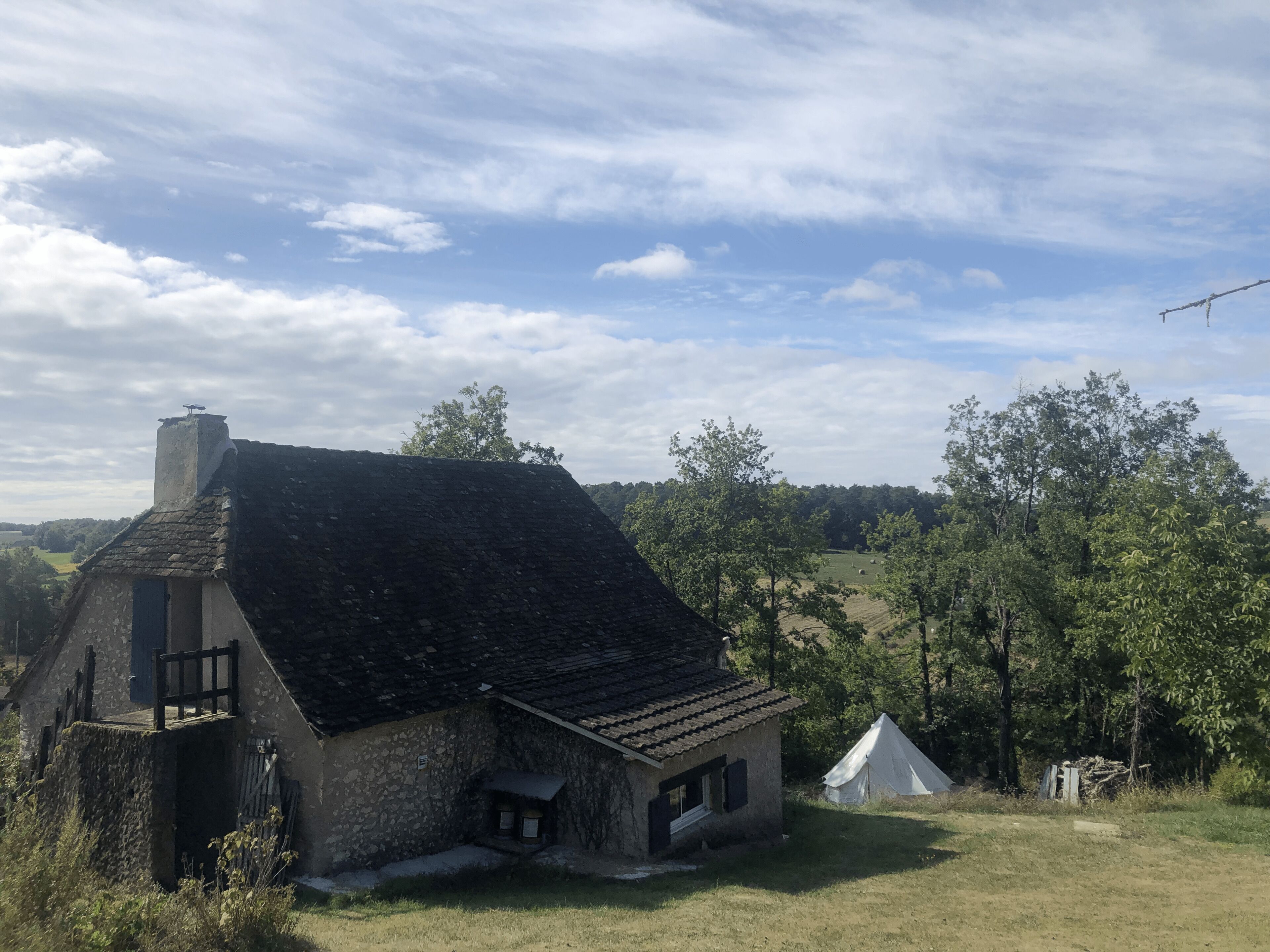 A rustic stone house with a sloped roof, a small porch, and a white tent nearby.