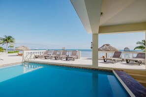Área da piscina com espreguiçadeiras e vista para a praia.