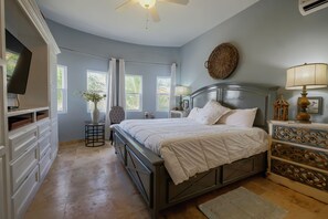 Quarto com cama, cômoda, televisão e janelas.