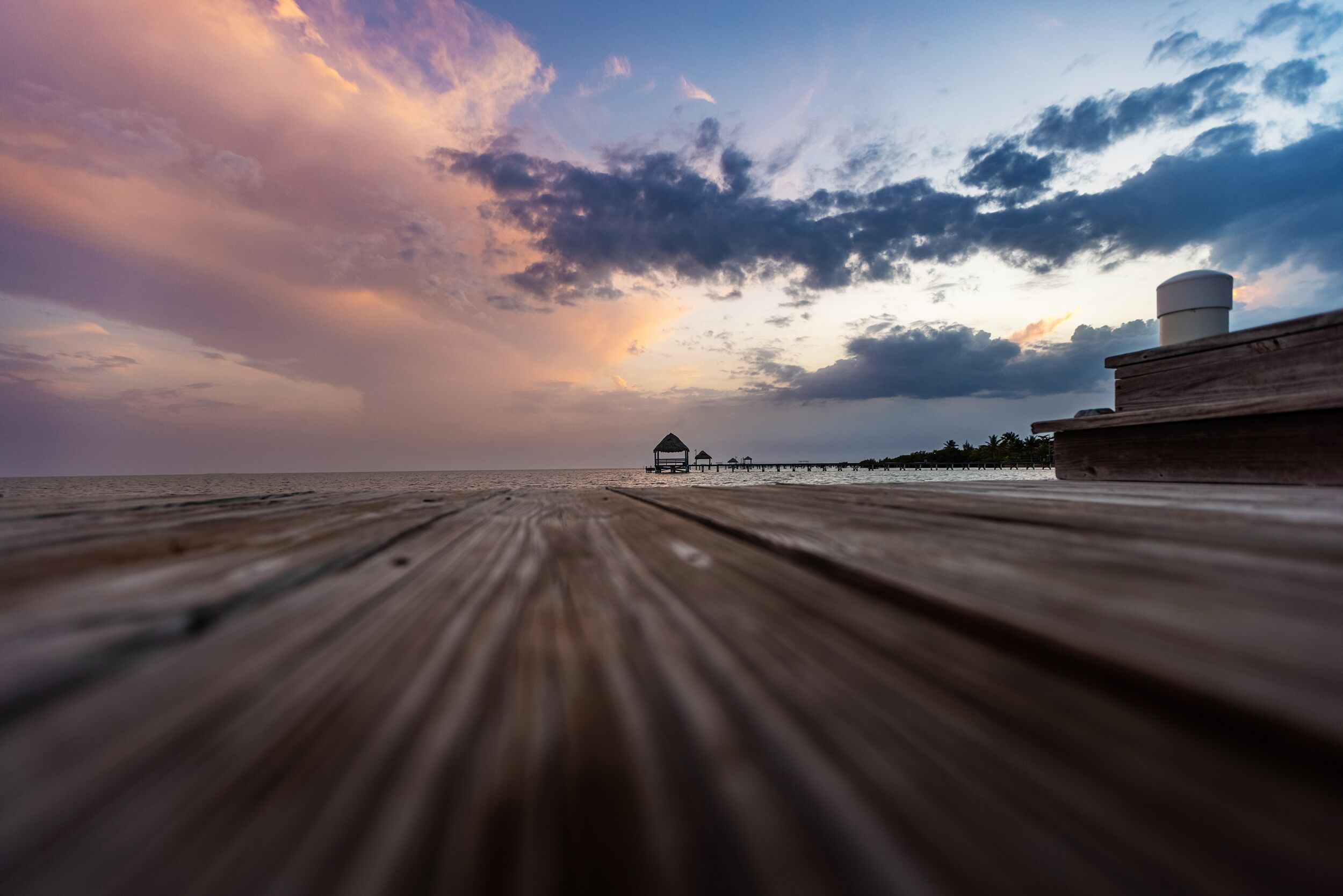 A wooden pier extending into the sea with a distant view of a structure on the horizon.