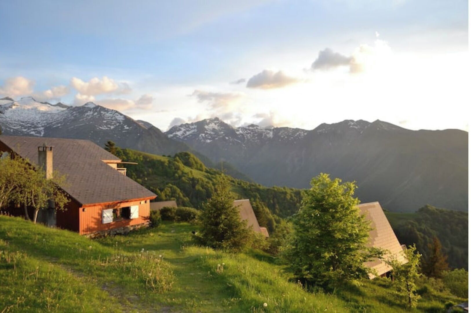 A rural setting with houses on a hillside, surrounded by mountains and greenery.