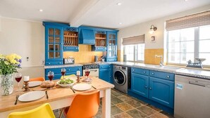 A modern kitchen with blue cabinets, a wooden dining table, and orange chairs.