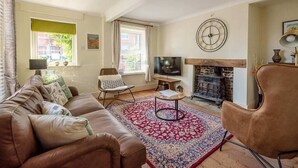A living room with a brown leather sofa, a patterned rug, a television, a fireplace, and a clock on the wall.