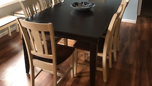 A dining room with a black table, six wooden chairs, a black bowl on the table, a wreath on the wall, and a framed painting. - Peaceful and private with quick access to all the Black Hills has to offer! (Rapid City)