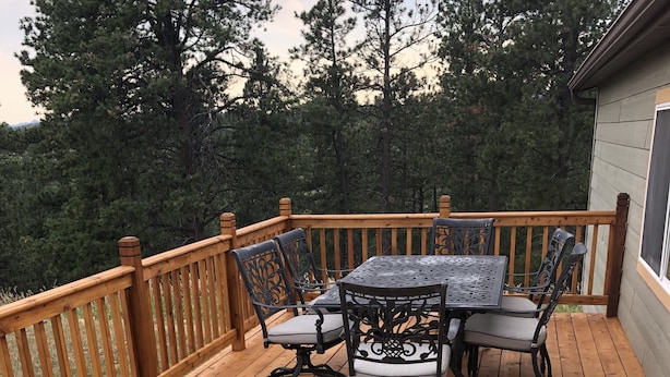 A wooden deck with a table and chairs, surrounded by a wooden railing. - Peaceful and private with quick access to all the Black Hills has to offer! (Rapid City)