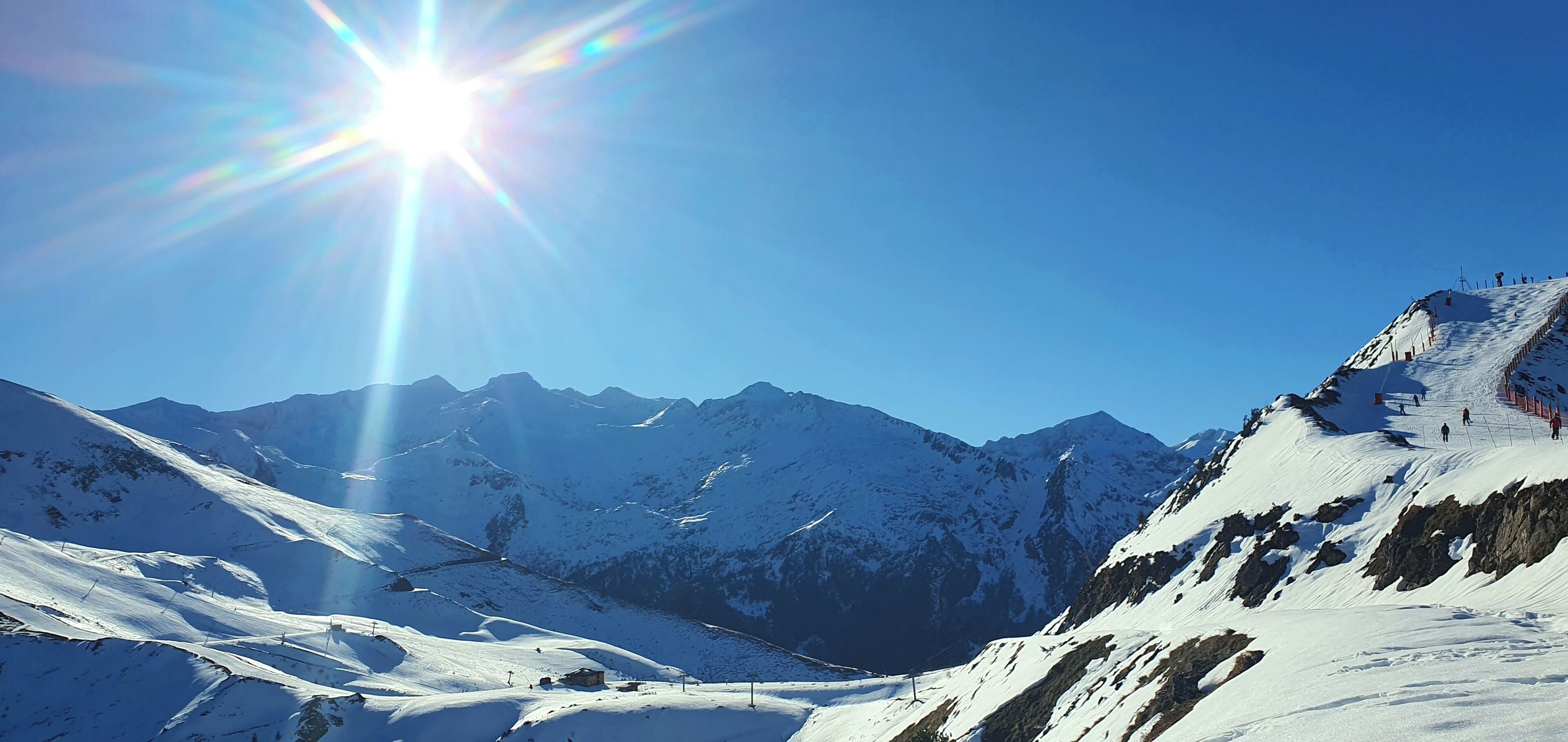 A snow-covered mountain landscape with a clear sky and sunlight.