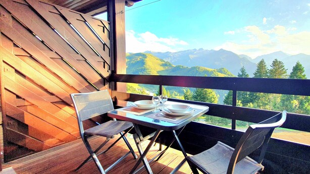 A balcony with a table set for two, overlooking a mountainous landscape.