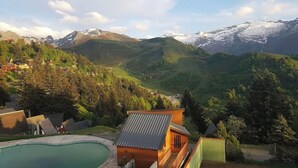 A mountain resort with a pool, wooden cabins, and a view of snow-capped peaks.