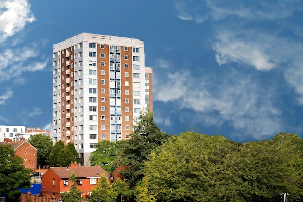 A high-rise apartment building with multiple balconies, surrounded by trees and other residential buildings.