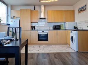 A compact kitchen with wooden cabinets, a built-in oven, a microwave, and a washing machine.