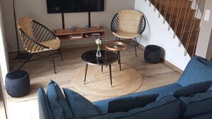 Ett modernt vardagsrum med en blå soffa, flätade fåtöljer, ett runt soffbord och en stor TV med platt skärm.