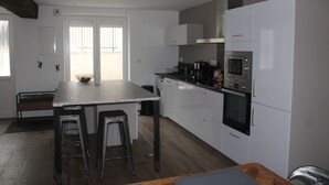 Ett modernt kök med en central köksö, barstolar, en inbyggd ugn och vita köksskåp.