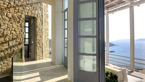 Un muro esterno in pietra, una porta in vetro e un balcone con vista sul mare.