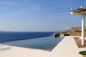 En infinitypool med fri utsikt över havet, ett trädäck och en stenmur.