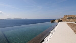 Una piscina a sfioro cristallina con un muro in pietra e un sentiero che conduce a un edificio in pietra.