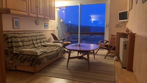 A cozy living area with a sofa, a small table, and chairs, a wooden cabinet, and a view through a glass door. - Appartement à 2 Minutes à Pied des Commerces et Télécabines Avec Superbe vue (Font-Romeu-Odeillo-Via)