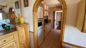 A kitchen with wooden cabinets, a tiled floor, and a wooden archway leading to another room. - Appartement à 2 Minutes à Pied des Commerces et Télécabines Avec Superbe vue (Font-Romeu-Odeillo-Via)