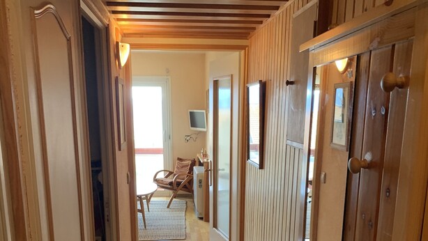 A wooden hallway with a ceiling of horizontal beams, leading to a room with a chair and a television. - Appartement à 2 Minutes à Pied des Commerces et Télécabines Avec Superbe vue (Font-Romeu-Odeillo-Via)