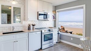 A modern kitchen with white cabinetry, a built-in oven, and a view of the beach. - Ocean Front with Beautiful Views! Miles of Sandy Beach! (Seal Rock)