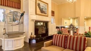A spacious lobby with a fireplace, a staircase with a birdcage, and a seating area with striped cushions.