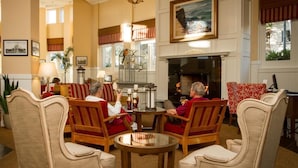 A cozy lounge area with wooden chairs and sofas, a fireplace, and a large painting on the wall.